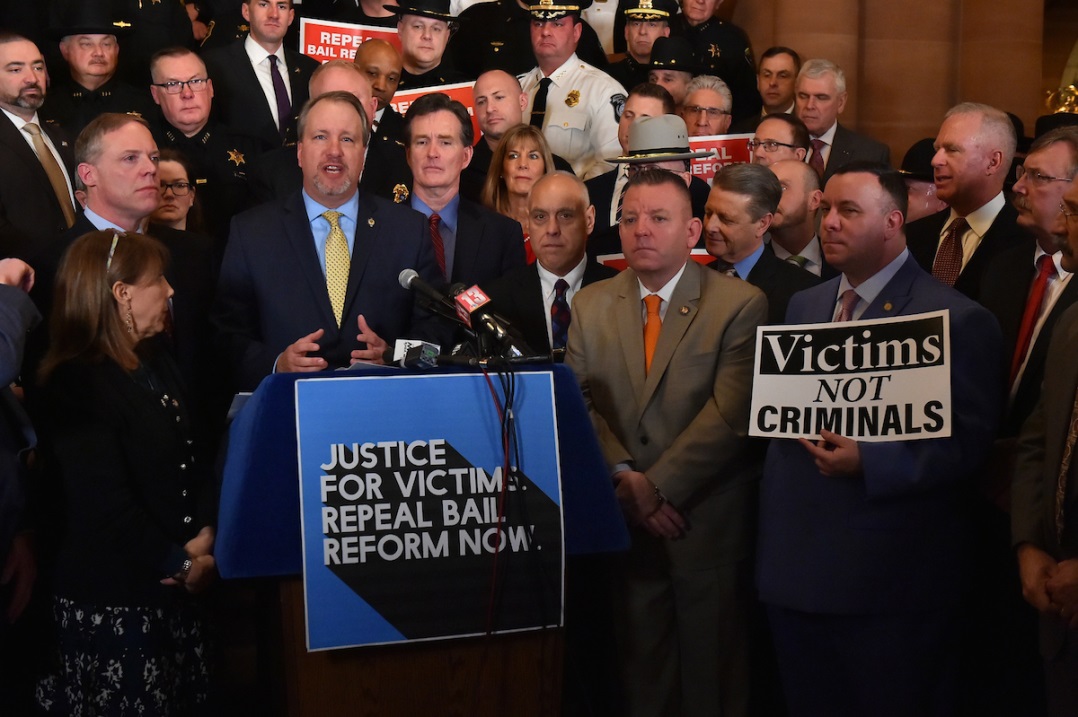 Assistant Minority Whip Karl Brabenec [holding sign front right] listens as Orange Co. District Attorney David Hoovler speaks on repealing new bail laws at a rally in Albany Tuesday, February 4.